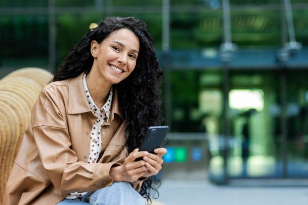 istock Young woman sitting outside on a bench using her smartphone 2107510497