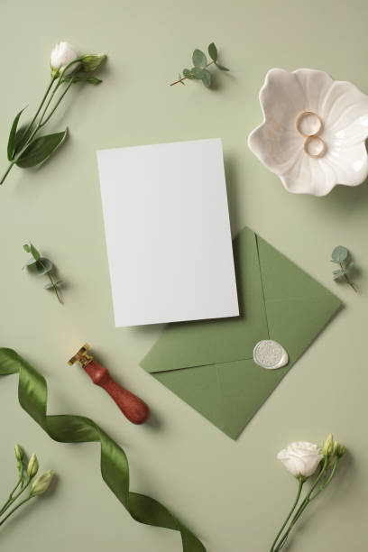 istock Flat lay composition with wedding invitation mockup, green envelope, wax stamp, flowers and gold rings on pastel green background. 2107513093