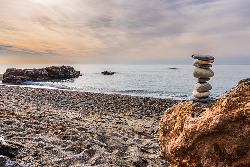 Tower created with beach stones, Apacheta, on a rock and with the Mediterranean Sea in the background.