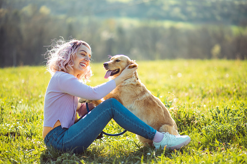 Woman with pink haircut has a fun in the nature with her golden retriever