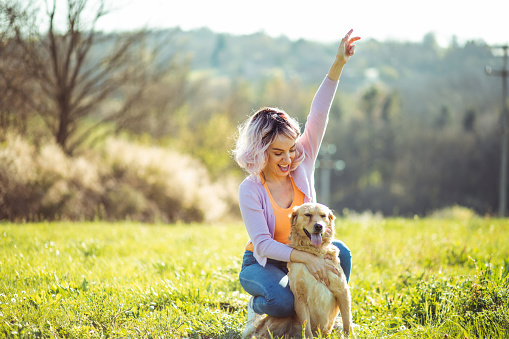 Woman with pink haircut has a fun in the nature with her golden retriever