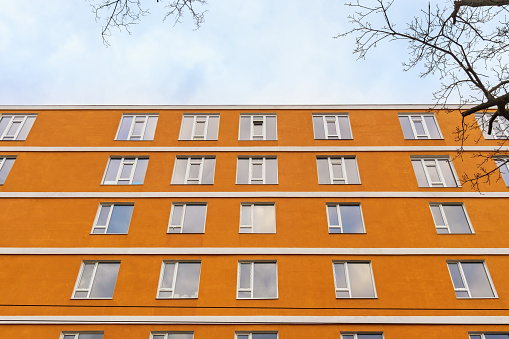 Facade of a modern multi-storey building with windows and an orange wall, bottom view