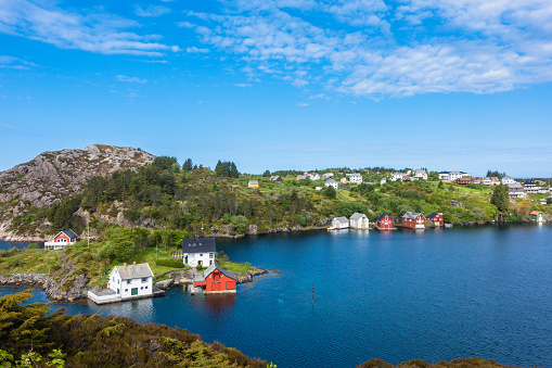 High view of a rural Nordic fishing village along the mountain range with colorful houses on partially clouded day with blue skies