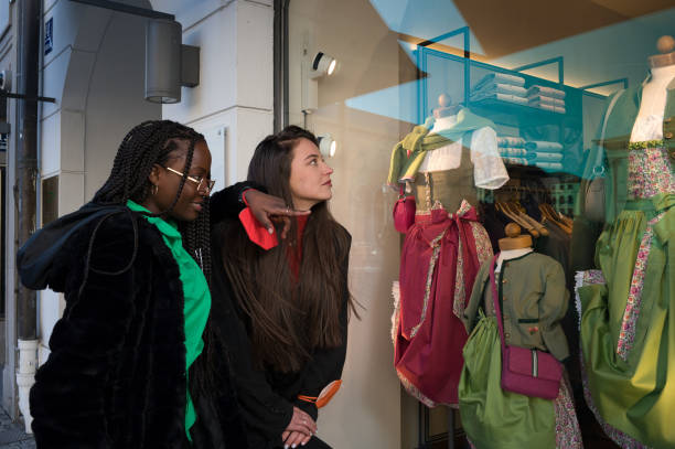 istock Nicely dressed young Caucasian- and African women having fun while watching shop-windows downtown wearing FFP2 mask on their wrists 2107682392