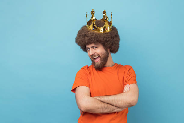 Man in golden crown, standing with crossed hands, looking at camera with funny expression.
