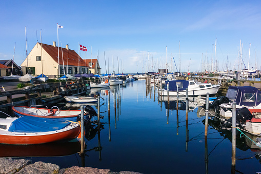 Danish marina dock area with vintage wooden and modern boats with Danish flag full mast in background on a mostly clear blue sky day with water reflections