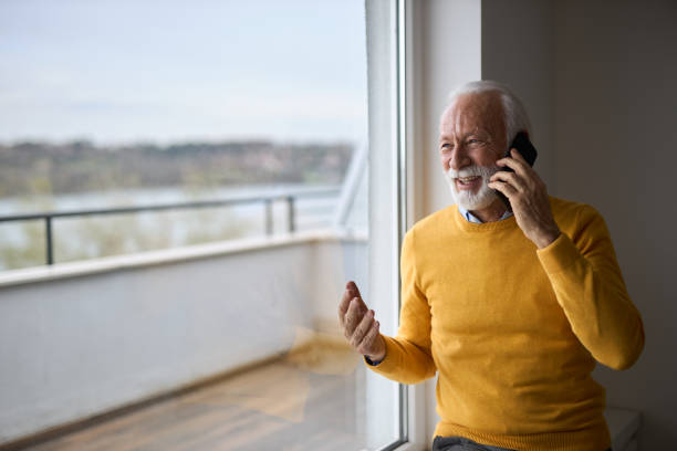 istock Happy mature man talking to someone over smart phone and looking through window 2107788468