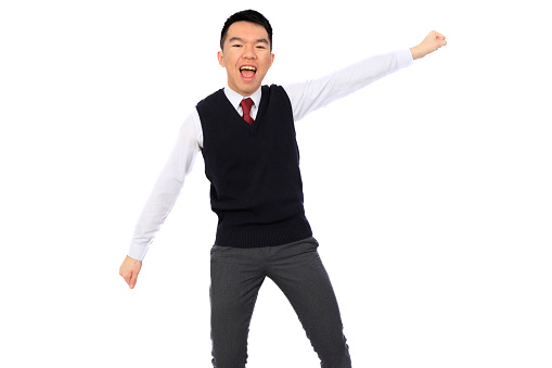 A young Asian high school student is giving a superhero takeoff pose with a big smile, representing success and celebration. He is wearing a black sweater vest over a white shirt and red tie. The background is white and isolated in a studio.