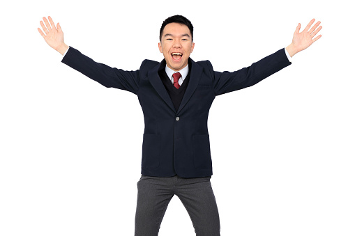 A young Asian businessman or high school or university student is posing with arms flailing and waving wide and smiling big at the camera. He is wearing his school uniform, a black blazer, with a suit and tie. The background is white and isolated in a studio.