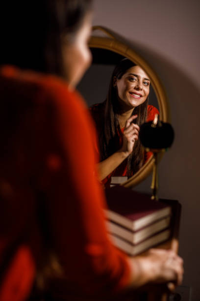 Selective focus shot of smiling young woman looking in the mirror and fixing her hair and make up when getting ready.