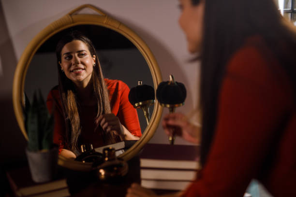 Selective focus shot of smiling young woman looking in the mirror and fixing her hair and make up when getting ready.