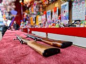 Two air rifles are ready for customers to use to shoot and are lying on a counter to be used in a shooting gallery at a fun fair carnival