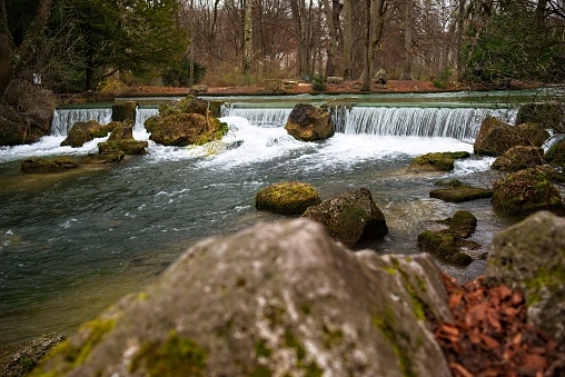 Tranquil river with small waterfall and moss-covered rocks surrounded by a serene forest landscape.