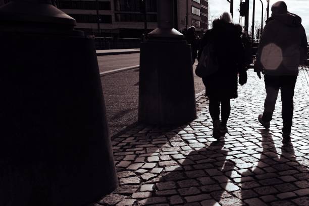 istock Silhouetted pedestrians walking on cobblestone street with shadows, urban setting. 2107946381