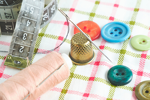 Sewing kit consisting needle, thimble, threads and measuring meter on a fabric background