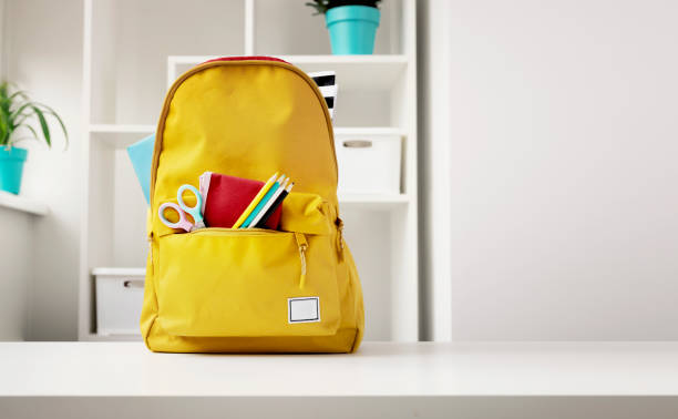 istock Yellow backpack with school accessories on table indoors. School supplies, objects. Back to school empty copy space background. 2108003658