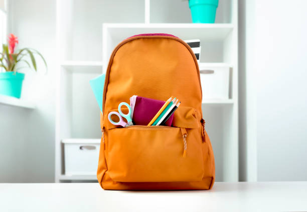 istock Orange backpack with school supplies on table indoors. 2108003663
