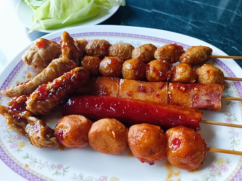 A plate of food with Crab sticks, meatballs and fish balls. The meatballs is covered in barbecue sauce.