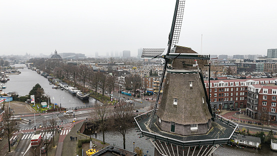 Aerial view of the windmill located at De Gooyer in Amsterdam, Aerial view to windmill in Amsterdam, Aerial view of famous windmill in Amsterdam, Traditional Windmill, Amsterdam Aerial View at sunrise with the canals\n\nDe Gooyer is a windmill in Amsterdam located between Funenkade and Zeeburgerstraat. It is the tallest wooden mill in the Netherlands at 26.6 meters high. It is registered as a National Monument.\n\nThe names dates from the around 1609, when the mill was owned by Claes and Jan Willemsz, two brothers from Gooiland. It is also known as \