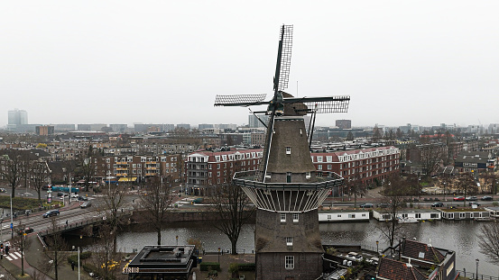 Aerial view of the windmill located at De Gooyer in Amsterdam, Aerial view to windmill in Amsterdam, Aerial view of famous windmill in Amsterdam, Traditional Windmill, Amsterdam Aerial View at sunrise with the canals\n\nDe Gooyer is a windmill in Amsterdam located between Funenkade and Zeeburgerstraat. It is the tallest wooden mill in the Netherlands at 26.6 meters high. It is registered as a National Monument.\n\nThe names dates from the around 1609, when the mill was owned by Claes and Jan Willemsz, two brothers from Gooiland. It is also known as \
