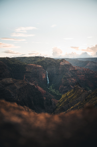 Witness the breathtaking beauty of Waimea Canyon in Kauai, Hawaii, as the first light of dawn bathes the landscape in a symphony of colors. This impressive image captures the iconic red earth tones of Waimea Canyon, accentuated by vibrant hues illuminated by the rising sun. Amidst this stunning panorama, the majestic Waipo'o Falls cascades down the canyon walls, adding to the enchanting scene. As Waimea Canyon reveals its grandeur during sunrise, the landscape becomes a mesmerizing display of nature's splendor. Immerse yourself in the awe-inspiring beauty of Kauai's natural wonders.