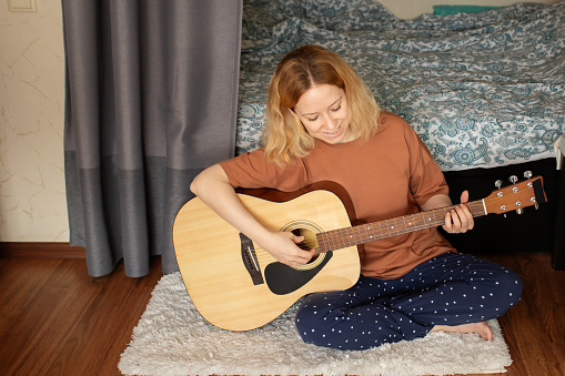 Woman playing guitar, home practice session, acoustic instrument, musical education