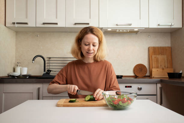 istock Culinary preparation, woman slicing cucumbers, kitchen cooking, fresh salad ingredients. 2108583901
