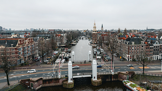 Aerial view of Montelbaanstoren Clock Tower in Amsterdam, Montelbaanstoren tower in Amsterdam, aerial city view of Montelbaanstoren Tower, aerial view of narrow canals of Amsterdam, popular place in Amsterdam

The Montelbaanstoren is a tower on bank of the Oudeschans – a canal in Amsterdam. The original tower was built in 1516 as part of the Walls of Amsterdam for the purpose of defending the city and the harbour. The top half, designed by Hendrick de Keyser, was extended to its current, decorative form in 1606. Since then the tower has been 48m tall.

Because the 3rd Duke of Alba proposed incorporating the tower into a castle (the Monte Albano) the tower became known in Dutch as the Monte Albano Toren. Over the years this became garbled to 