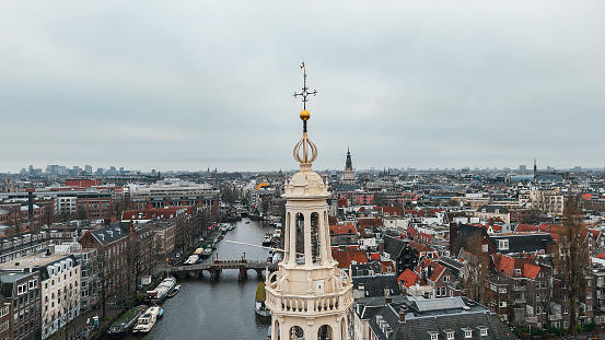 Aerial view of Montelbaanstoren Clock Tower in Amsterdam, Montelbaanstoren tower in Amsterdam, aerial city view of Montelbaanstoren Tower, aerial view of narrow canals of Amsterdam, popular place in Amsterdam\n\nThe Montelbaanstoren is a tower on bank of the Oudeschans – a canal in Amsterdam. The original tower was built in 1516 as part of the Walls of Amsterdam for the purpose of defending the city and the harbour. The top half, designed by Hendrick de Keyser, was extended to its current, decorative form in 1606. Since then the tower has been 48m tall.\n\nBecause the 3rd Duke of Alba proposed incorporating the tower into a castle (the Monte Albano) the tower became known in Dutch as the Monte Albano Toren. Over the years this became garbled to \