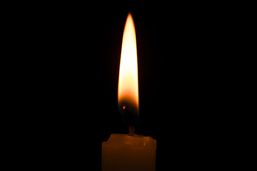 Closeup isolated candle glowing in pitch darkness.
