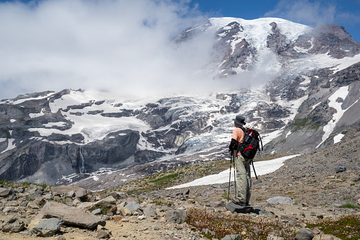 Man hiking Skyline Trail in Mount Rainier National Park. Mt Rainier peeking through the clouds. Washington State.