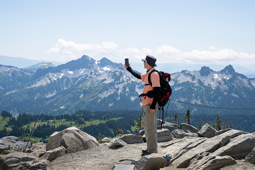 Hiker taking selfie photos using a smartphone at Skyline Trail. Mt Rainier National Park. Washington State.