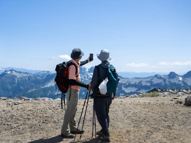 istock Hikers taking selfie photos using a smartphone at Skyline Trail. Plastic bag with rubbish on backpack. Take your garbage home concept. Mt Rainier National Park. Washington State. 2108619420