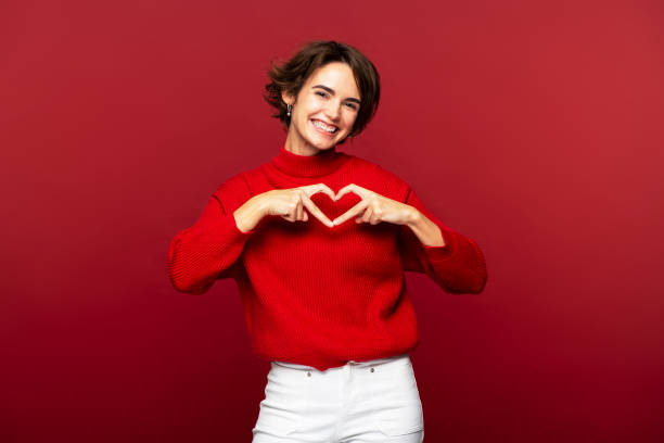 istock Woman making a heart gesture with her fingers, posing isolated on a red background 2108621184