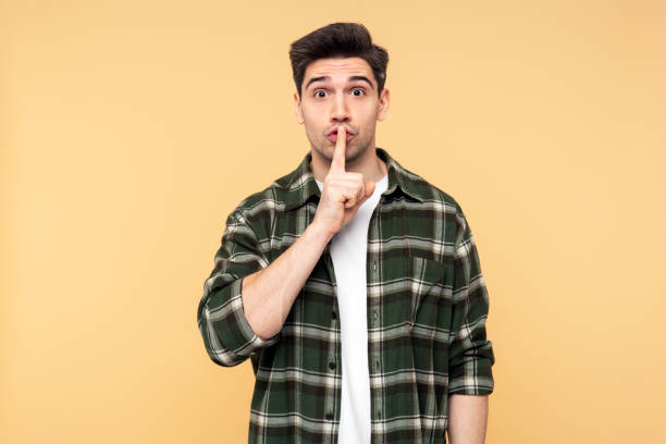 istock Man gesturing silence with his forefinger, wearing a checkered shirt, and looking directly at camera 2108622145