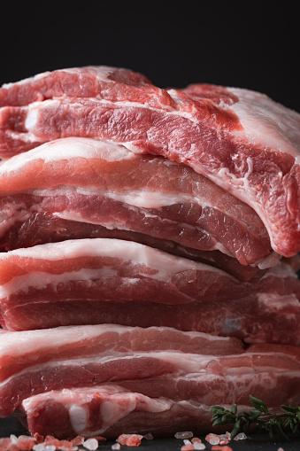 Close up shot of raw uncooked sliced pork meat surrounded by salt crystals, garlic and spices on the black background. Copy space for a free text. Cooking meat dishes recipe template.