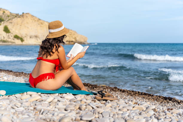 istock Young plus size girl in bikini reading a book on the beach 2108633520