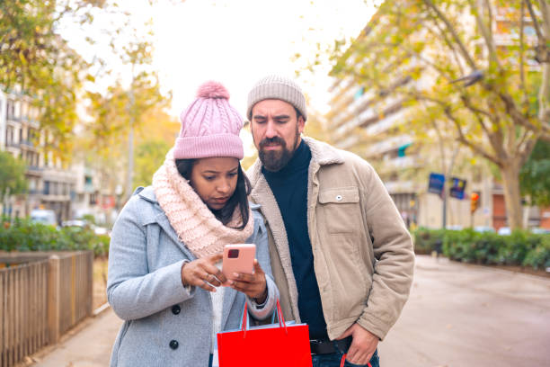 istock Smiling young multiracial couple holding shopping bags, browsing smartphone apps. 2108638210