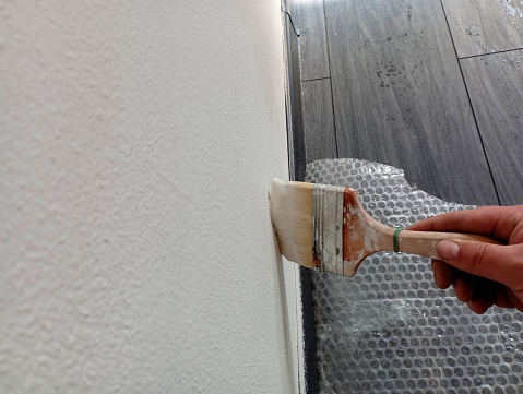 The topic of repair. Painting the wall in white with a wide brush. Independent repair of the walls in the room.