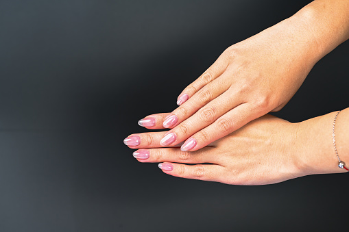 Hands of a beautiful woman on a dark background. Hands are delicate, nails natural, skin clean. Light pink nails.