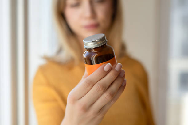 Young woman is holding a blank medicine bottle and pointing at it with her finger