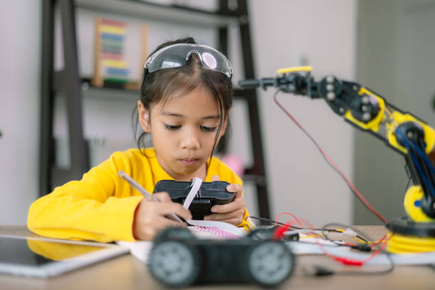 istock A young girl is sitting at a table with a robot and a remote control 2108678639