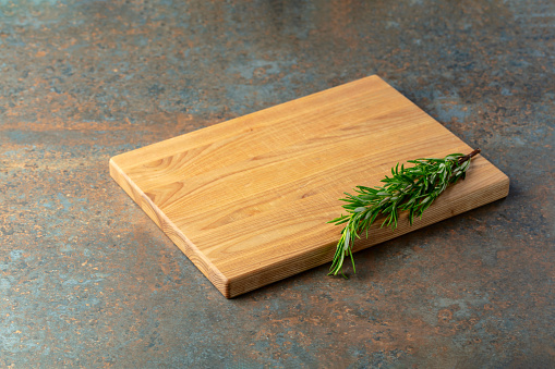 Cutting board and rosemary on a rusty iron table. Culinary background. Empty wooden cutting board, product display space.