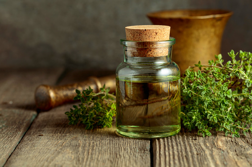 Bottle of thyme essential oil with fresh thyme twigs on an old wooden table.