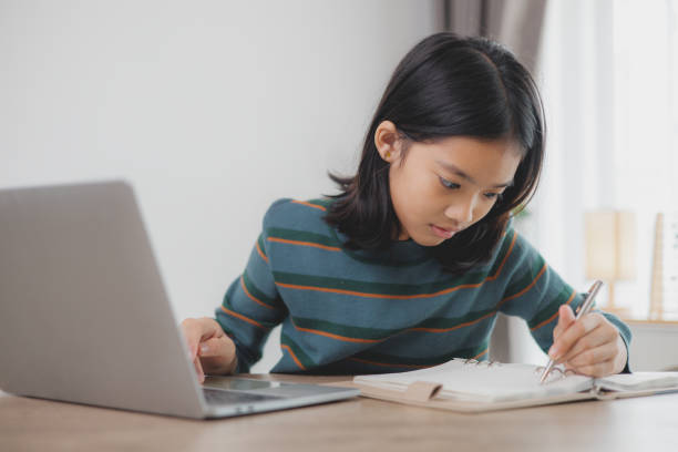 istock A girl is writing in a notebook while sitting at a table with a laptop 2108696501