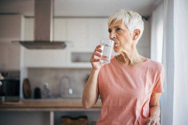 istock Senior woman drinks water and enjoys by the window 2108724698