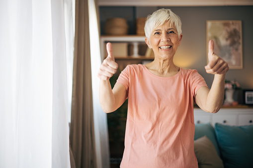 Portrait of a beautiful mature woman showing thumbs up in her living room