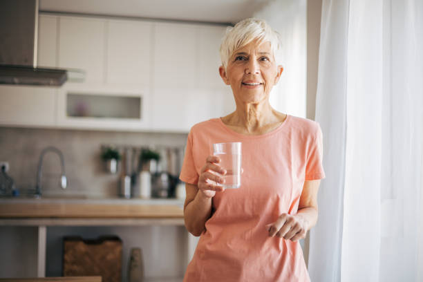 istock Senior woman drinks water and enjoys by the window 2108745178