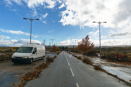 Camper van at an abandoned parking lot besides street with greenery and trees, Andalusia, Spain