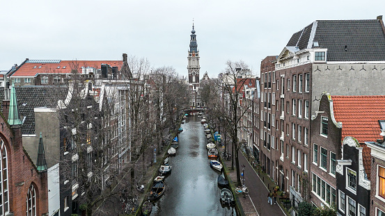 Amsterdam / Netherlands : Aerial view over a canal with the focus on the canal houses standing next to another. View with al lot of details. Residential area in the city center,  without people. In the background the old church tower.